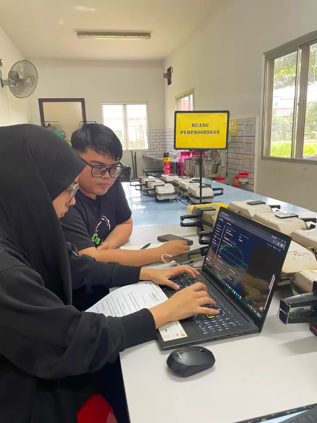 Two team members reviewing NakHalal on a laptop inside a food processing room.